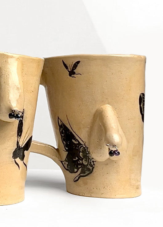 Two beige ceramic mugs with body designs and butterfly illustrations on a white background